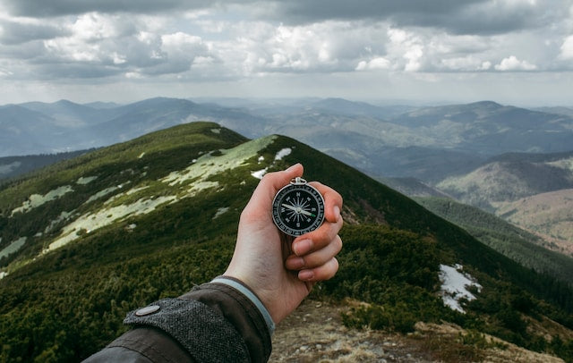 hand holding a compass with a cloudy mountain in the background