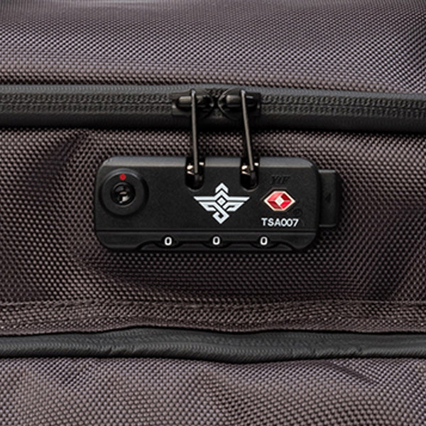 Close-up of a black TSA-approved suitcase lock with two zipper pulls attached, featuring the label TSA007 and a keyhole on textured fabric.