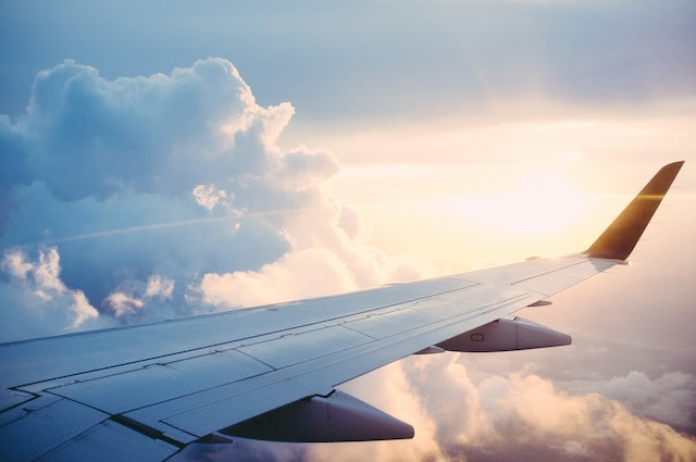 the wing of a plane with a cloudy sunrise in the background