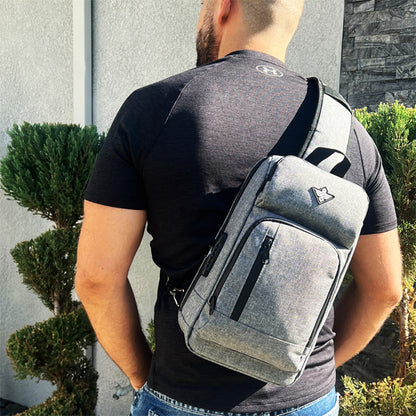 A man stands outdoors near trimmed bushes and a stone wall, wearing the Erozul Equinox Smell Proof Sling Bag With Combination Lock over his right shoulder.