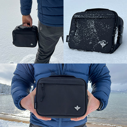 A person displays the Erozul Exodus Smell Proof Case With Combination Lock, featuring a white logo, outdoors by a snowy lakeside.